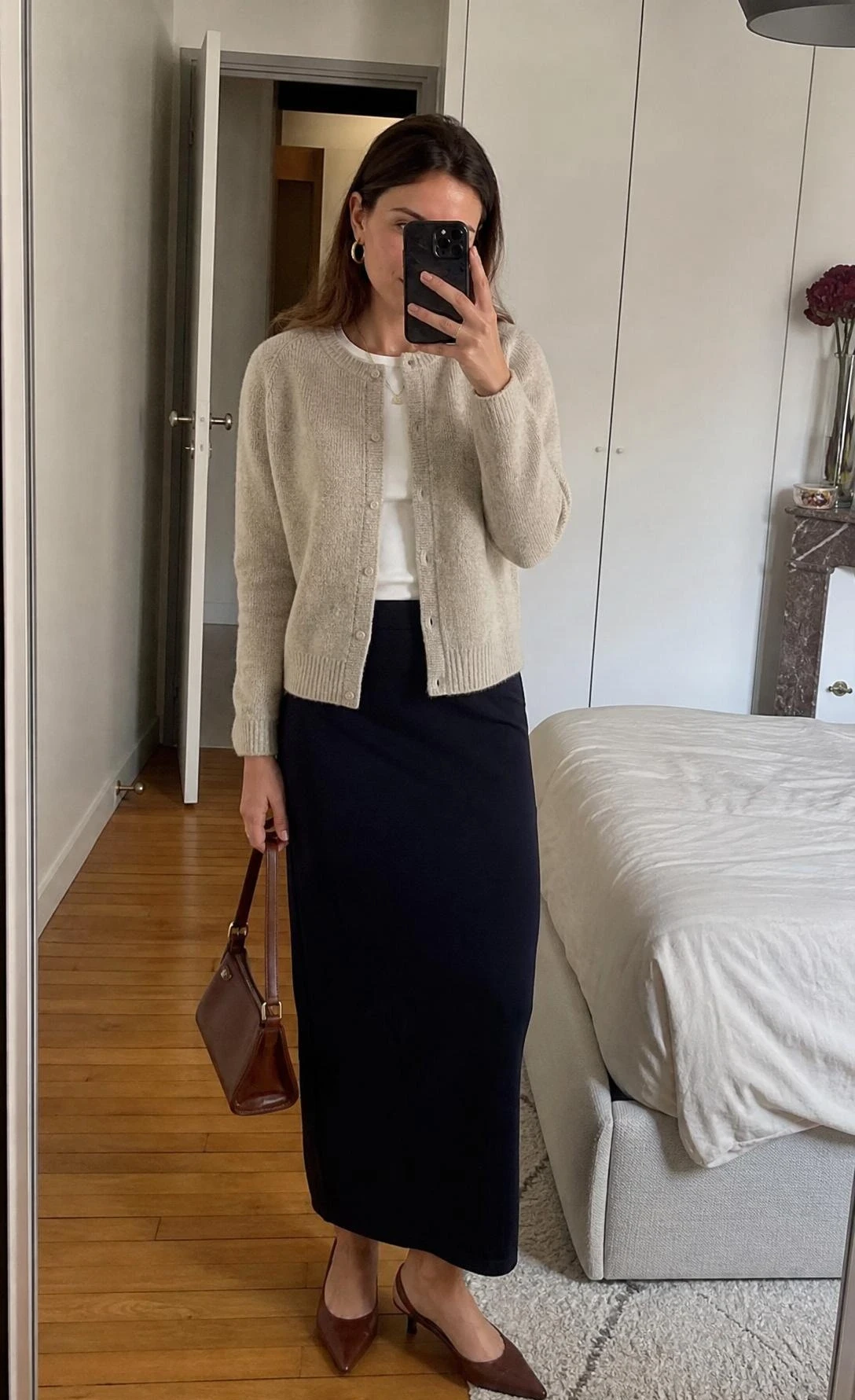 Mirror selfie of a woman in a fine knit cardigan and ankle-length column skirt, a chic parisian office outfit indoors.