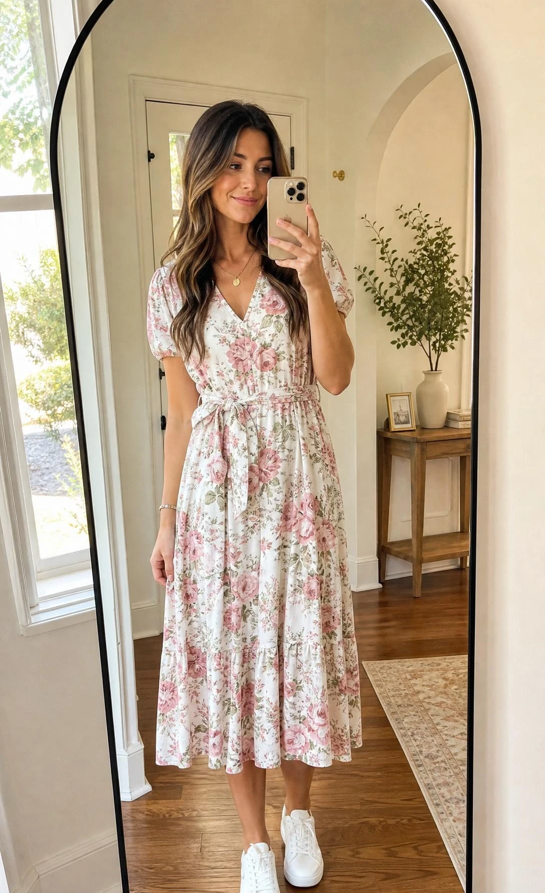 Young woman in a floral midi dress paired with crisp white sneakers takes a mirror selfie in a sunlit entryway, showing a casual yet polished brunch outfit