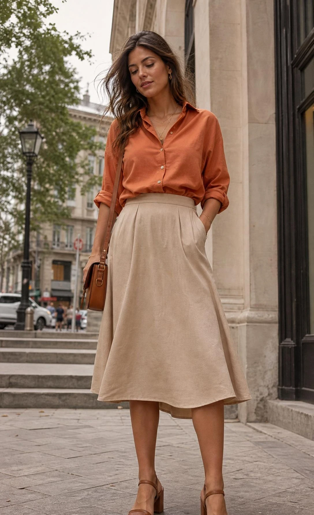 Woman wearing a muted terracotta orange button-down shirt tucked into a midi skirt, styled as a polished orange button down shirt outfit on an urban sidewalk