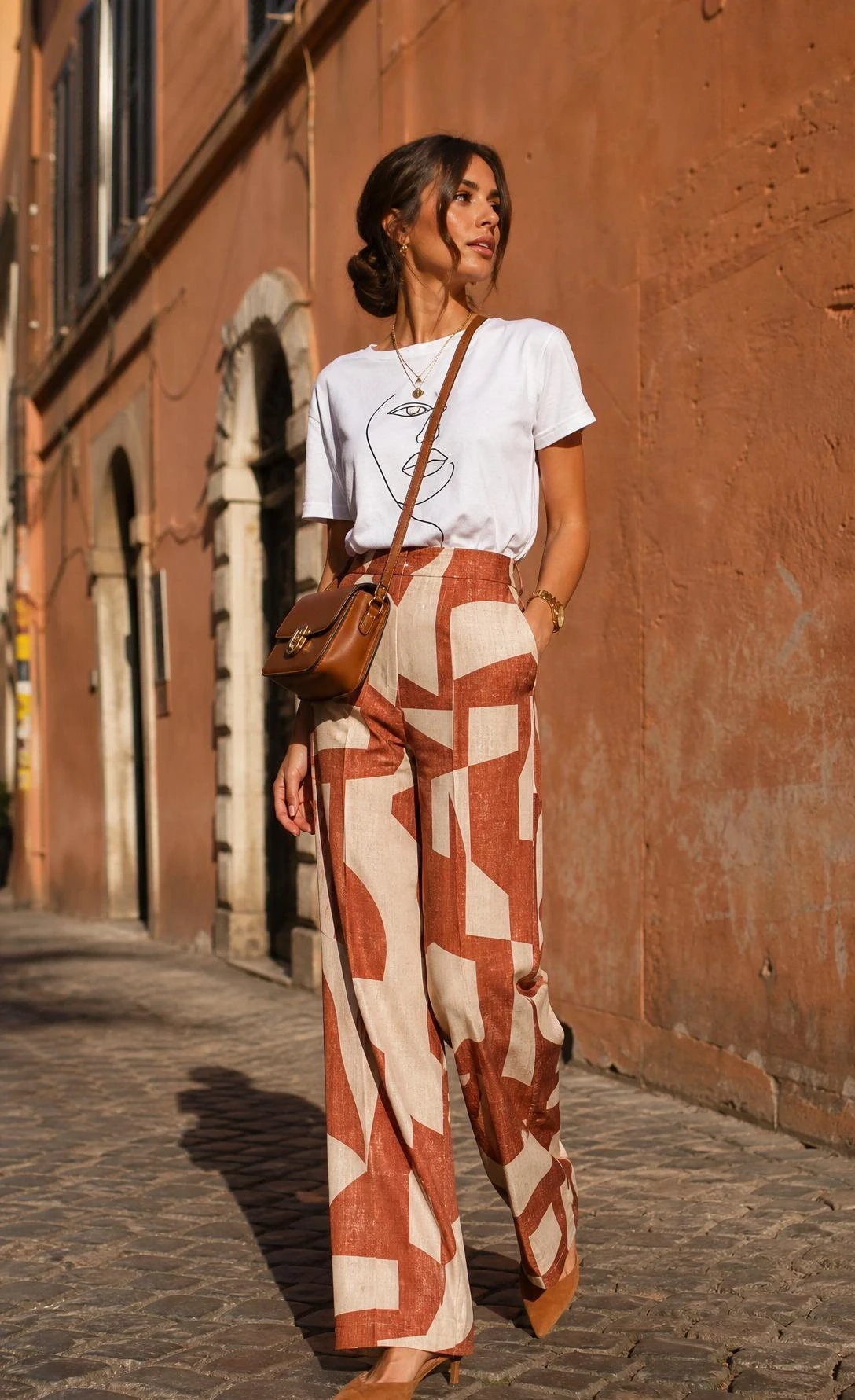 Tailored wide-leg patterned trousers paired with a simple graphic tee, styled for effortless street chic on a sun-lit cobblestone European street