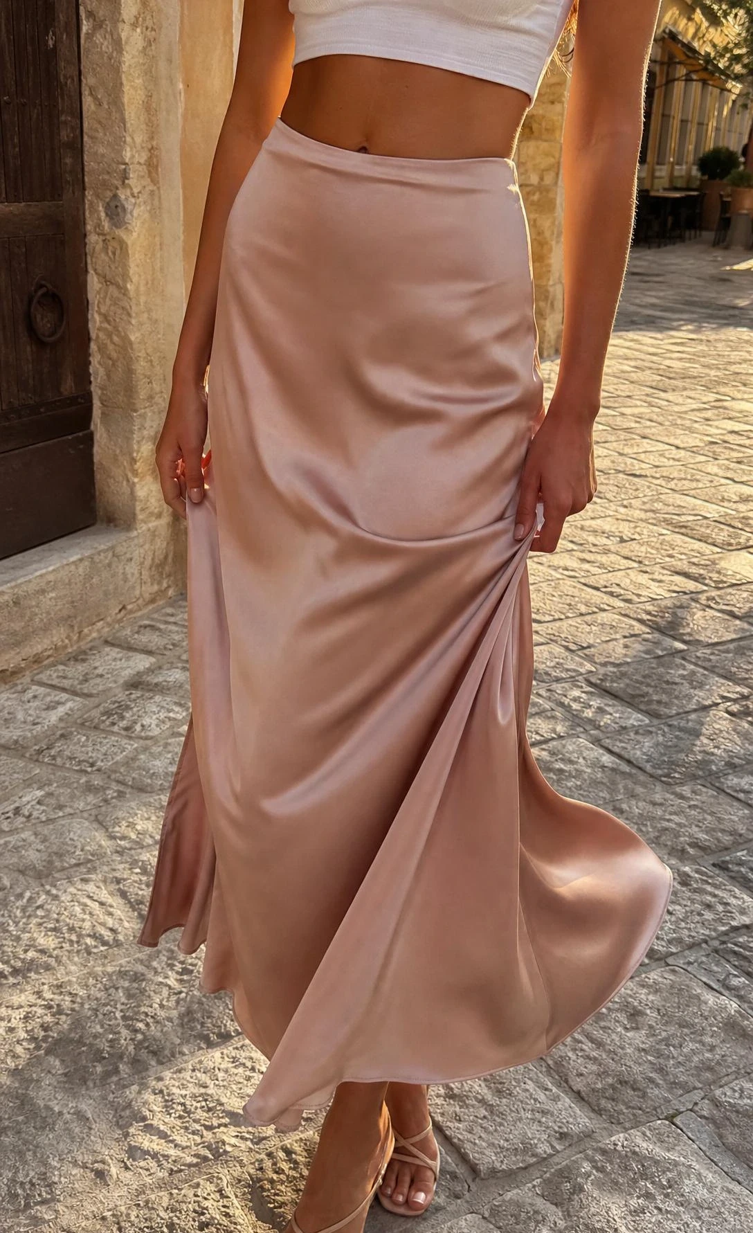 Satin maxi skirt in champagne paired with a white cropped tee, waist-down shot showing the luxurious fabric drape in warm afternoon light