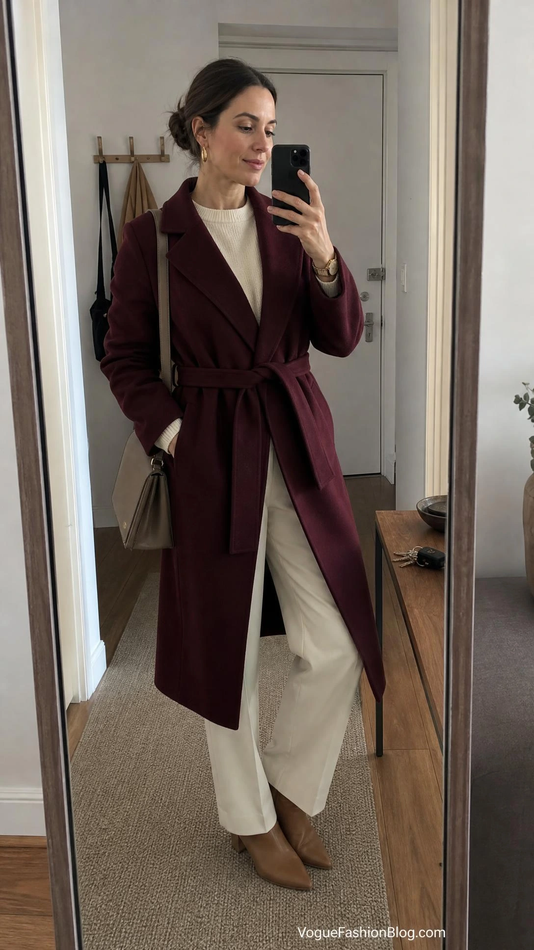 Woman in a burgundy coat and cream basics takes a mirror selfie in an apartment entryway, one of 2026 fresh fall outfit ideas