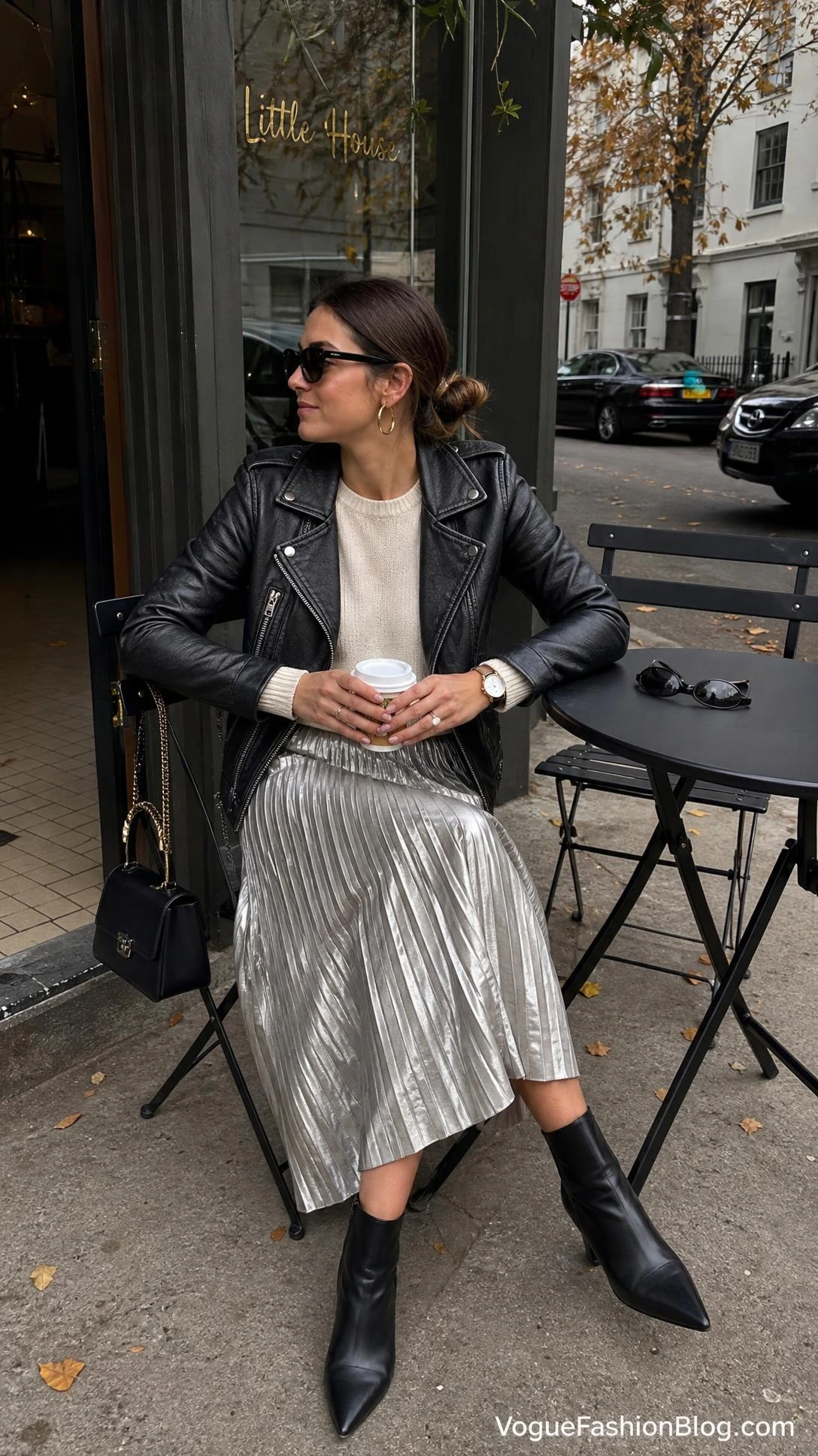 Woman at an autumn sidewalk café in a black leather jacket and metallic pleated skirt, among pleated midi skirt outfit ideas for fall