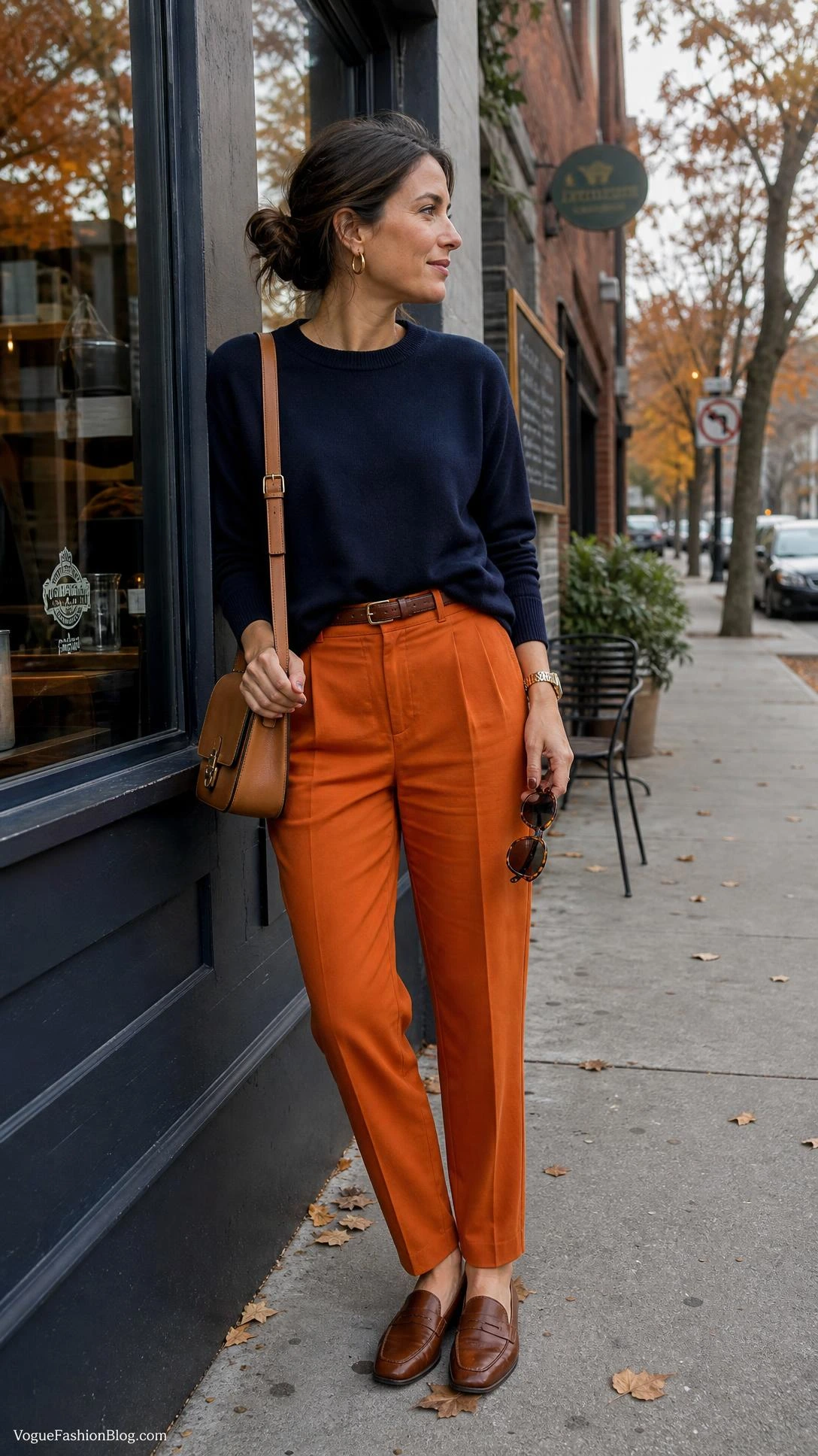 Woman in persimmon trousers and a navy sweater outside a café, a polished take on Persimmon Orange Outfit Ideas for Fall