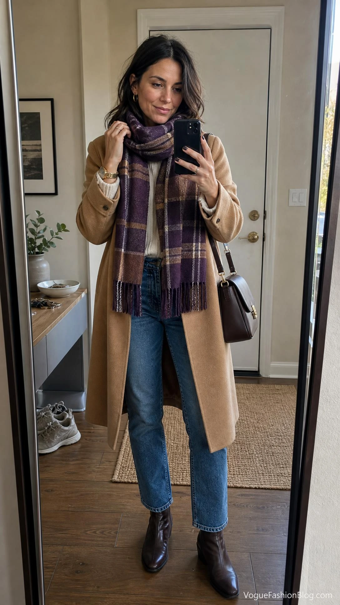 Woman taking a mirror selfie in a camel coat, denim jeans, and purple plaid scarf for royal purple outfit ideas this fall