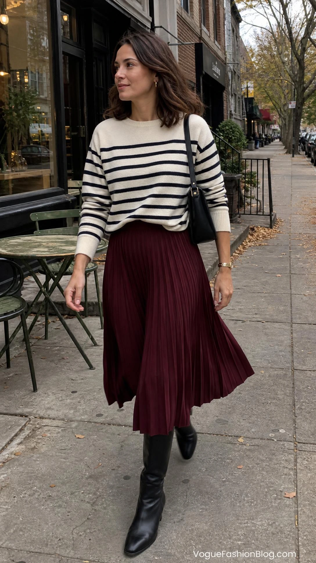 Woman in a striped knit and burgundy skirt walking past a café, styled for pleated midi skirt outfit ideas for fall
