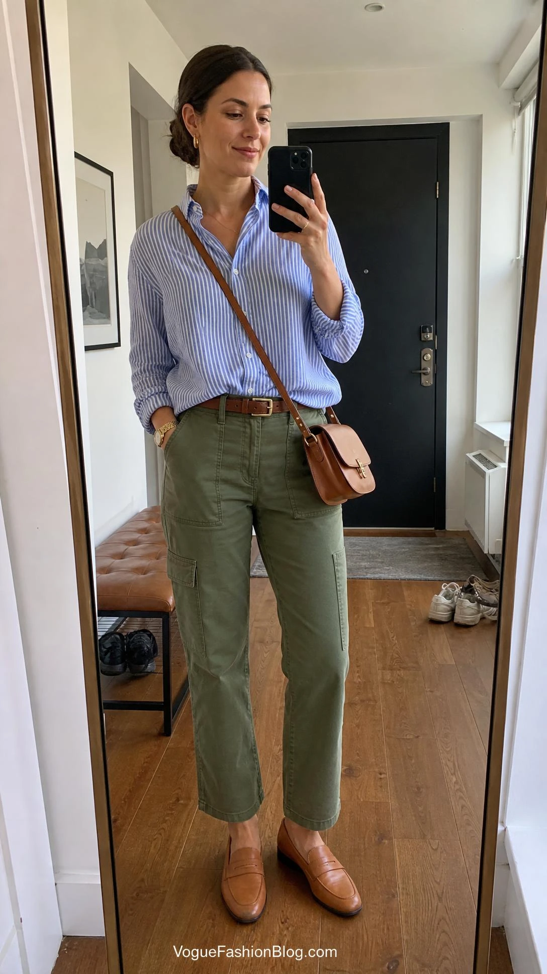 Woman in a blue-and-white button-down and olive utility pants takes an entryway mirror selfie for early fall striped shirt outfits