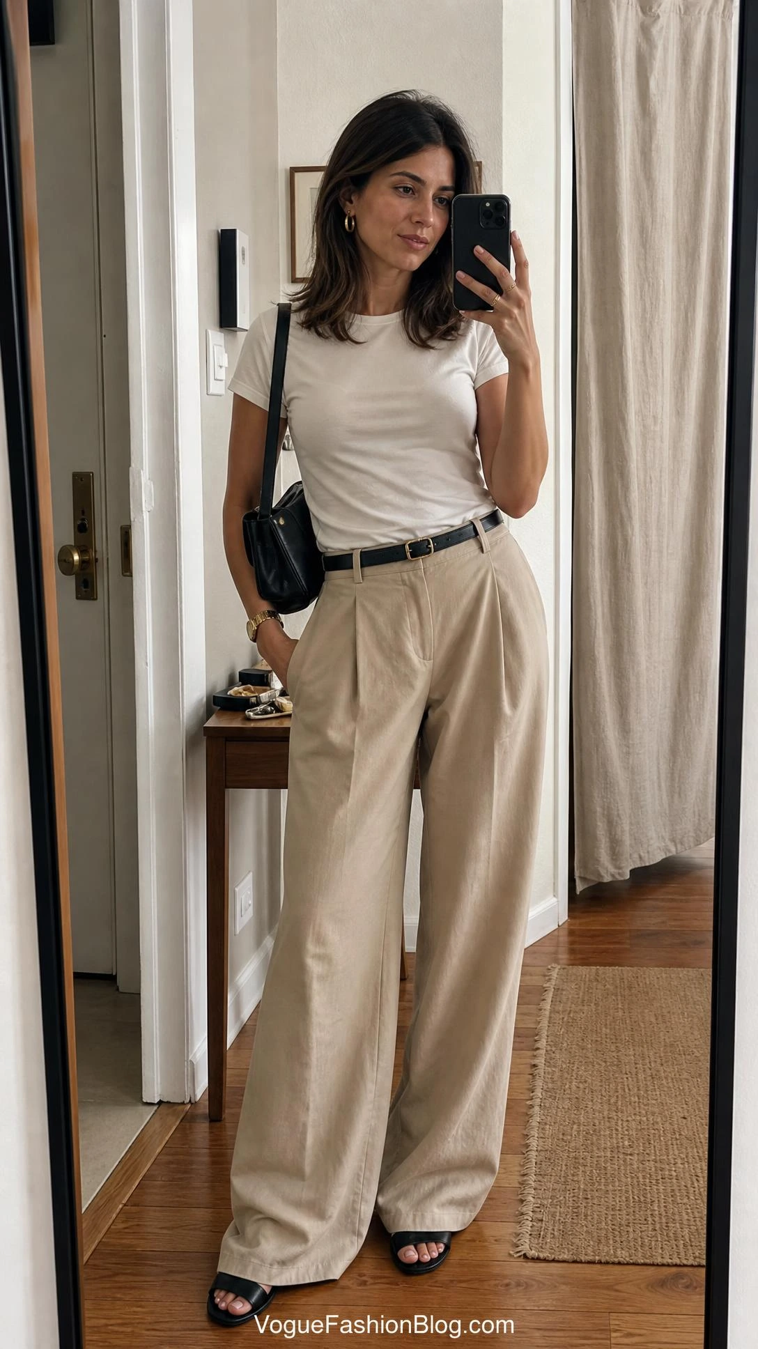 Woman in beige wide-leg trousers and a simple tee takes an entryway mirror selfie for late summer outfit ideas women.