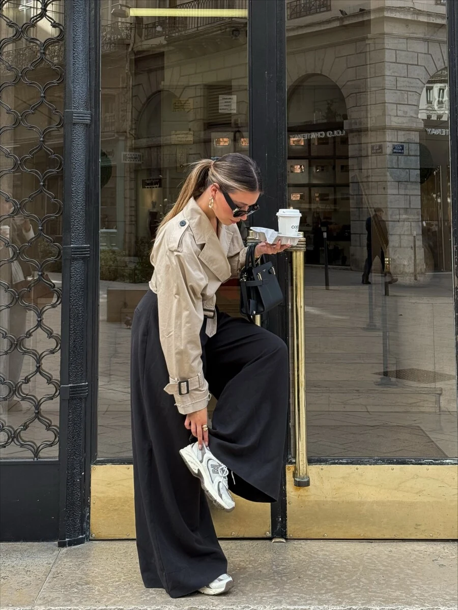 Cropped neutral trench jacket styled with black wide-leg pants and sneakers for a minimal fall look.