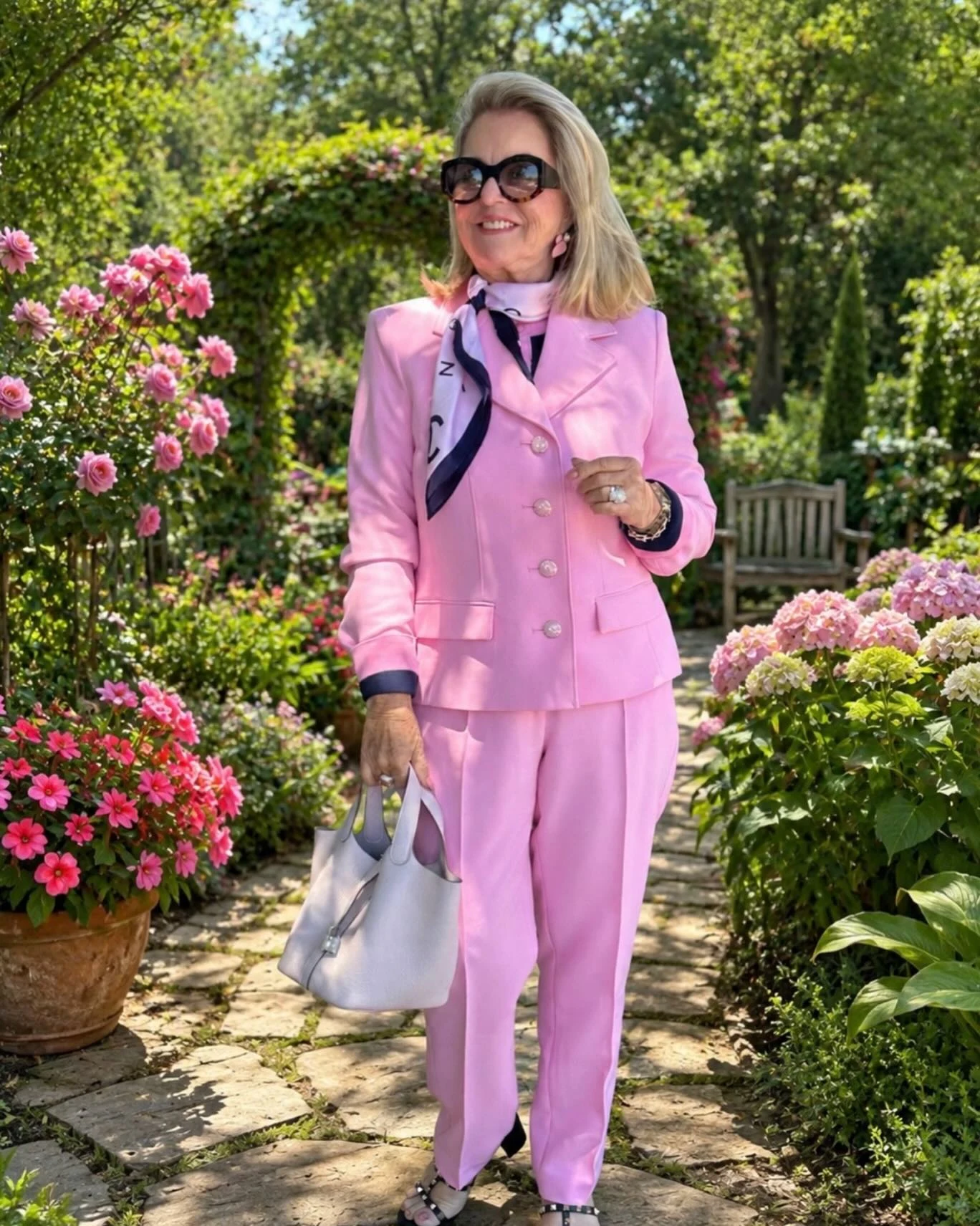 Woman wearing a pastel pink tailored blazer, wide-leg trousers, silk neck scarf, and tortoiseshell sunglasses.