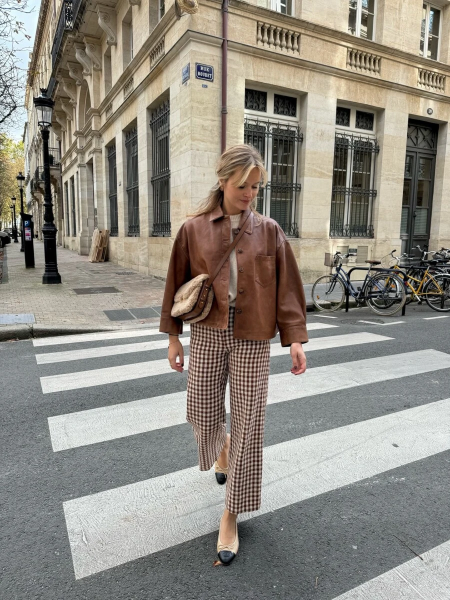 Woman in brown leather jacket and checked trousers crossing a Paris street in fall.