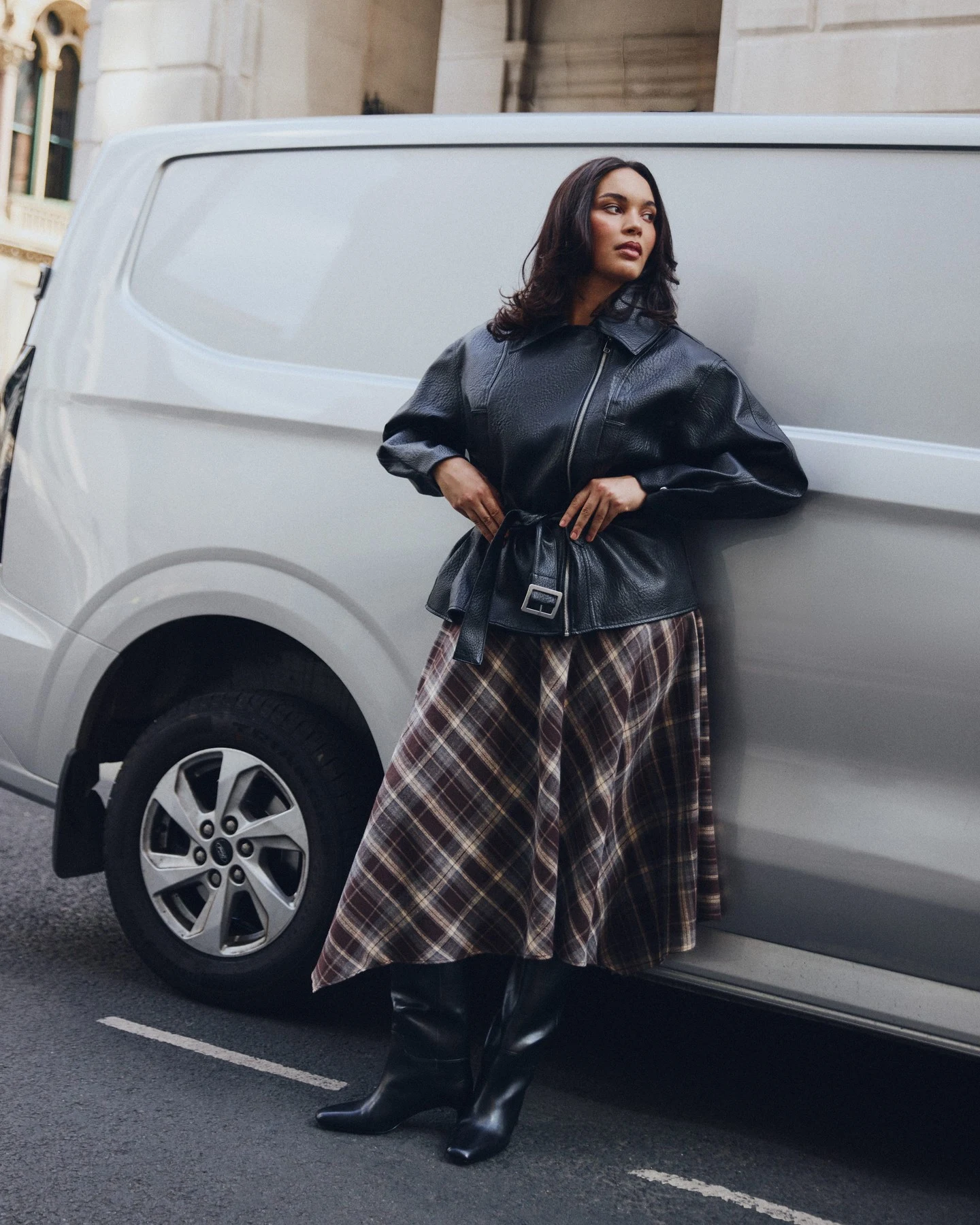 Plus size model in brown tartan midi skirt, black turtleneck, and knee boots in a 90s fall outfit.