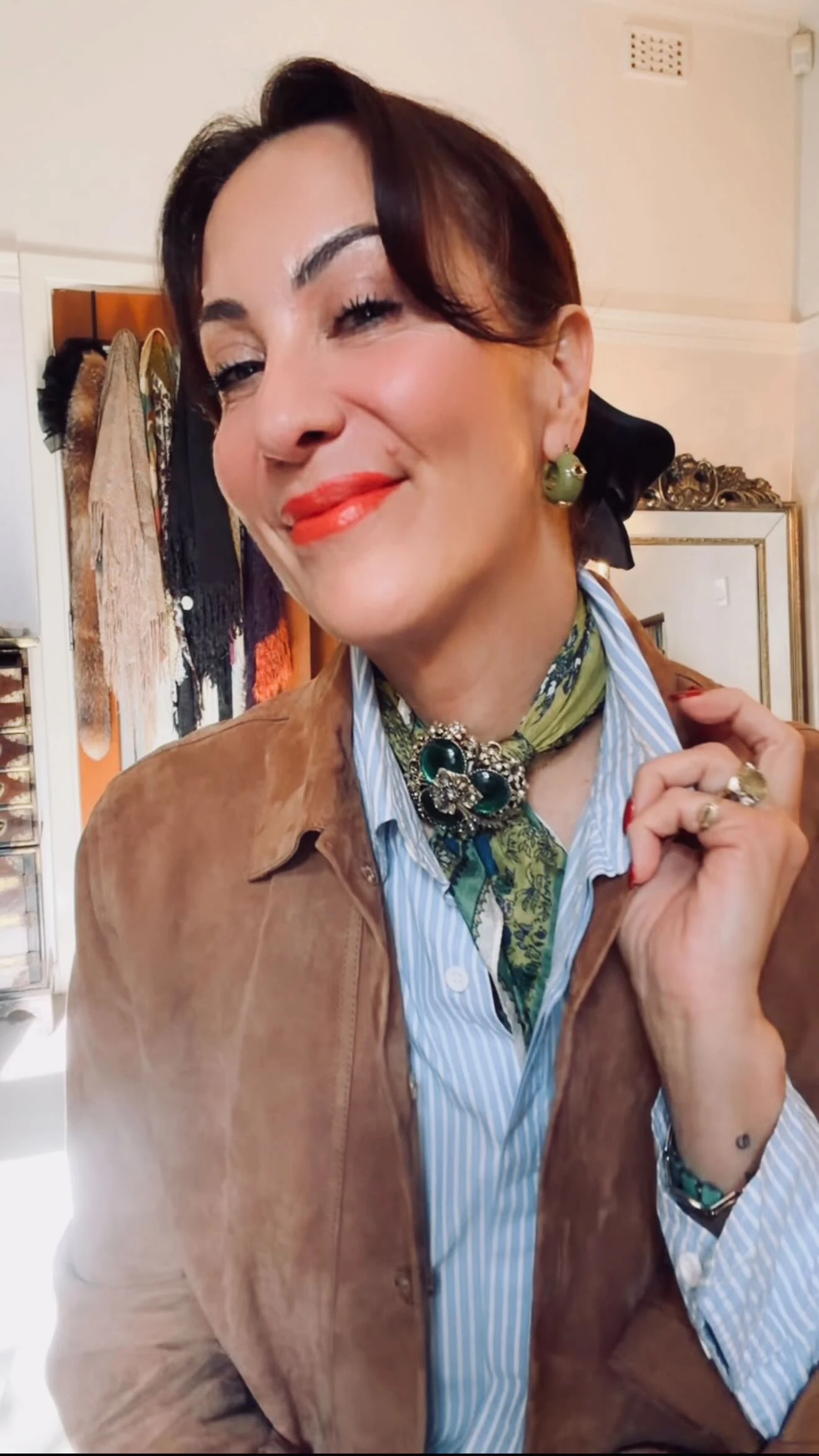 Striped shirt and suede jacket with silk neck scarf pinned by a green ornate brooch.