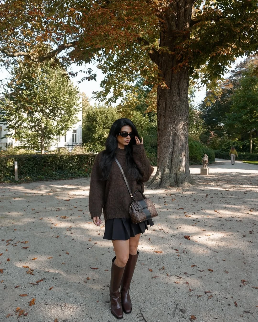 Oversized brown fuzzy sweater, black pleated mini skirt, tall brown knee-high boots, monogram crossbody bag.