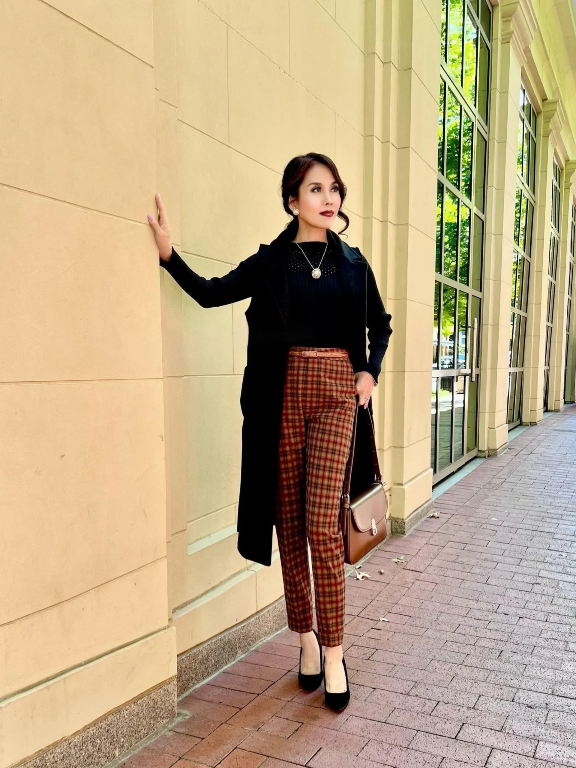 Black long coat, plaid high-waisted trousers, ribbed knit top, pointed heels, and brown structured shoulder bag.