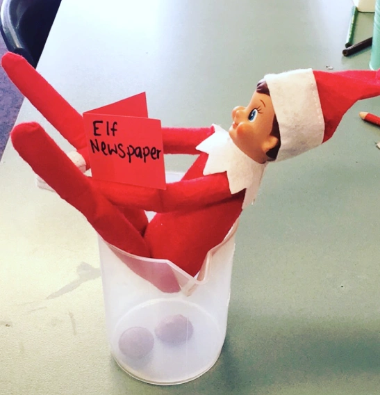 Charming Red Elf in a Clear Container with ‘Elf Newspaper’