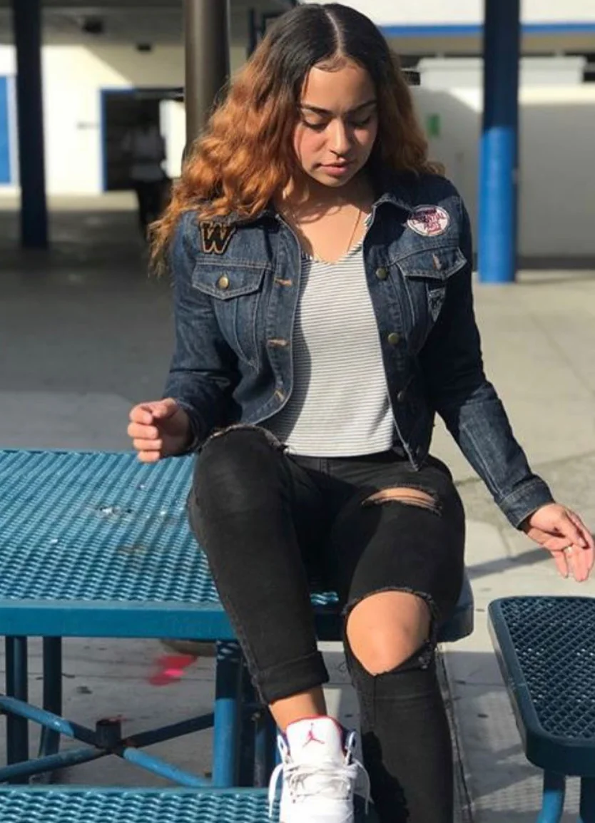Dark Wash Denim Jacket With Patches + Light Gray Ribbed Knit Top + Black Ripped Skinny Jeans + White Athletic Sneakers