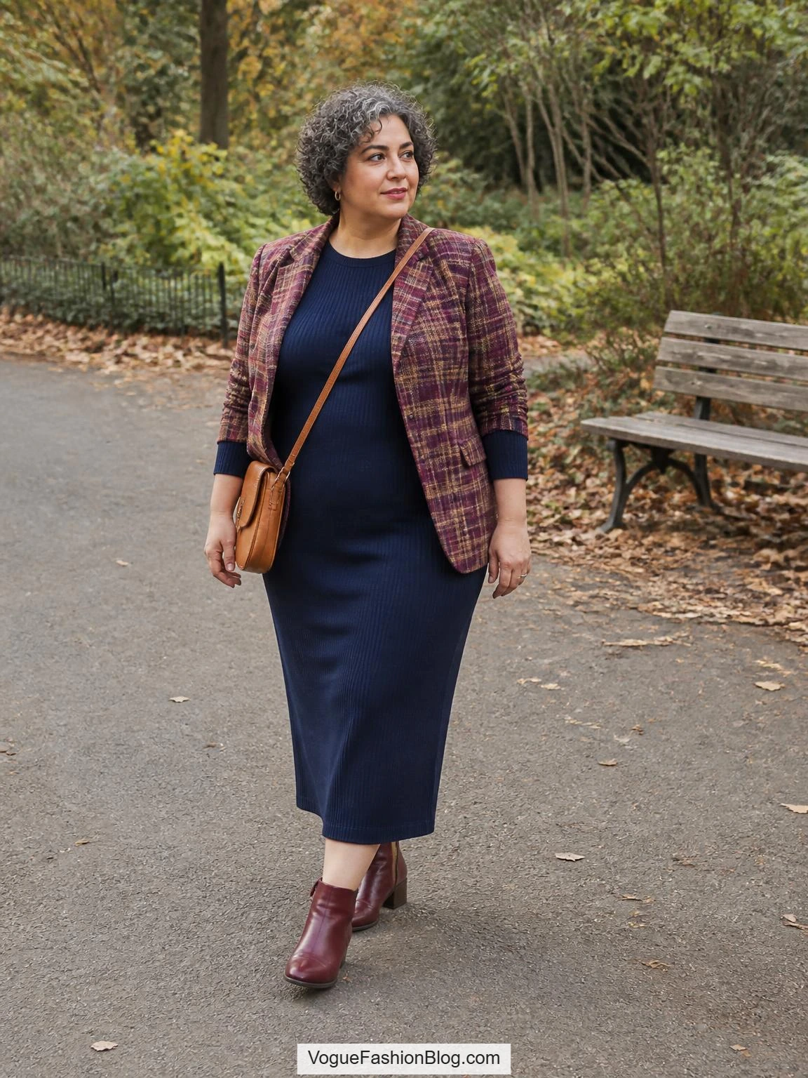 Plus size fall outfits feature a woman in a navy knit column dress, checked blazer, burgundy boots, and tan crossbody bag on a park path