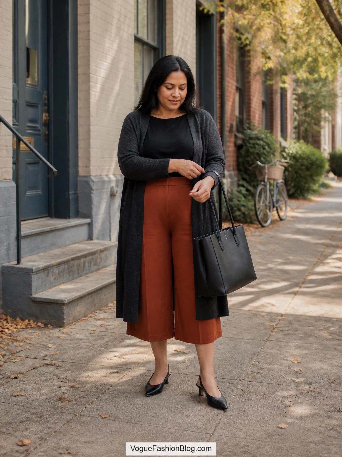 Plus-size fall outfits feature a woman styling terracotta culottes with a long charcoal cardigan on a residential sidewalk