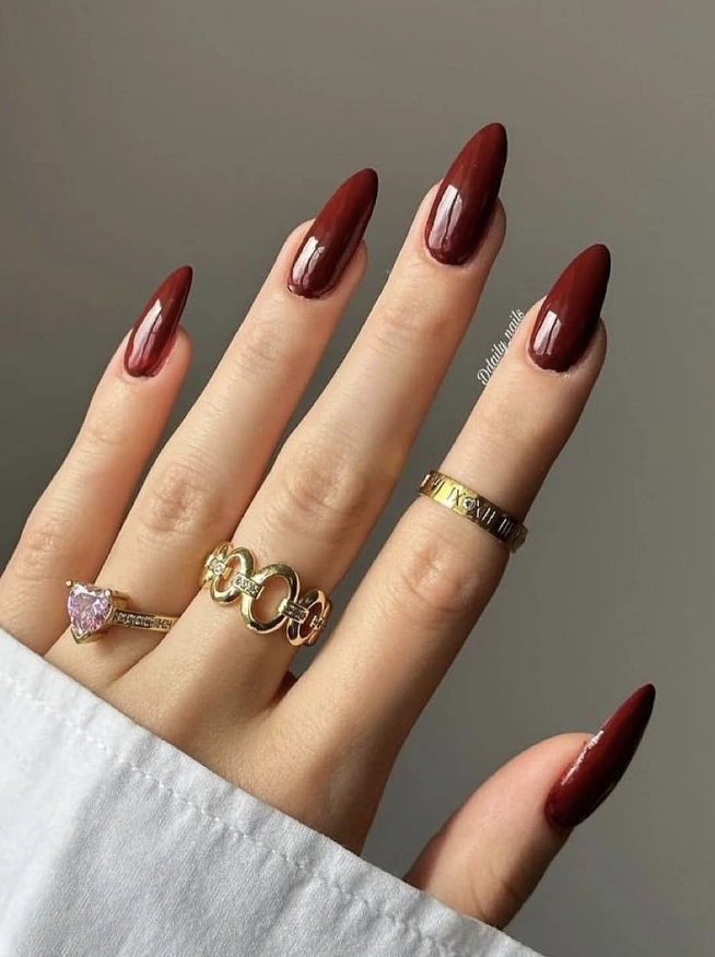 Elegant Burgundy Stiletto Nails with a Glossy Finish and Gold Jewelry Accents