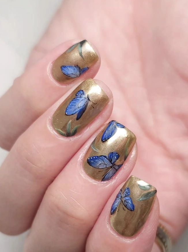 Shimmery Gold Nails with Delicate Blue Butterfly Decals